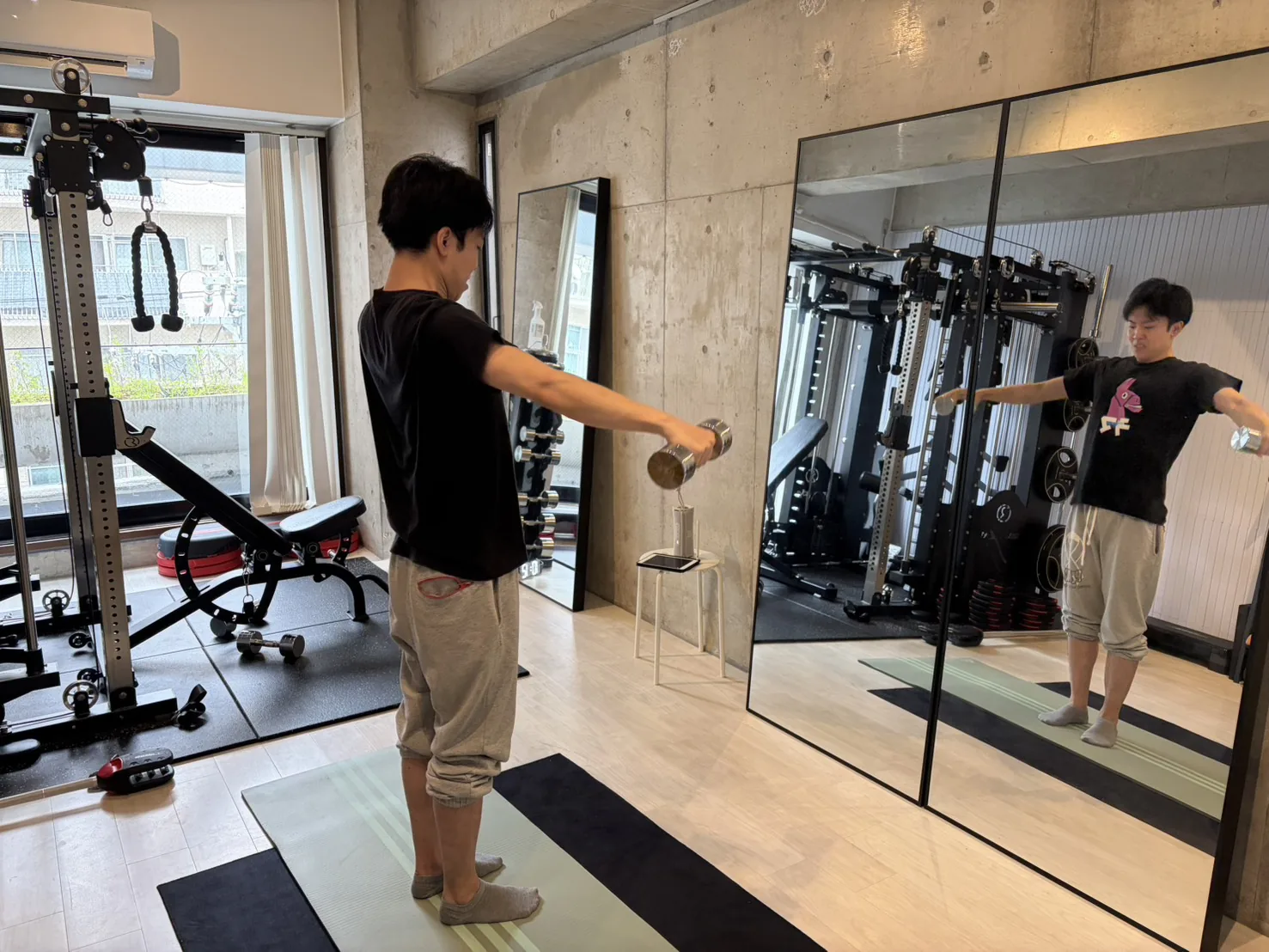 鏡張りのスタジオでダンベルを使いフォームを確認しながらトレーニングする様子
