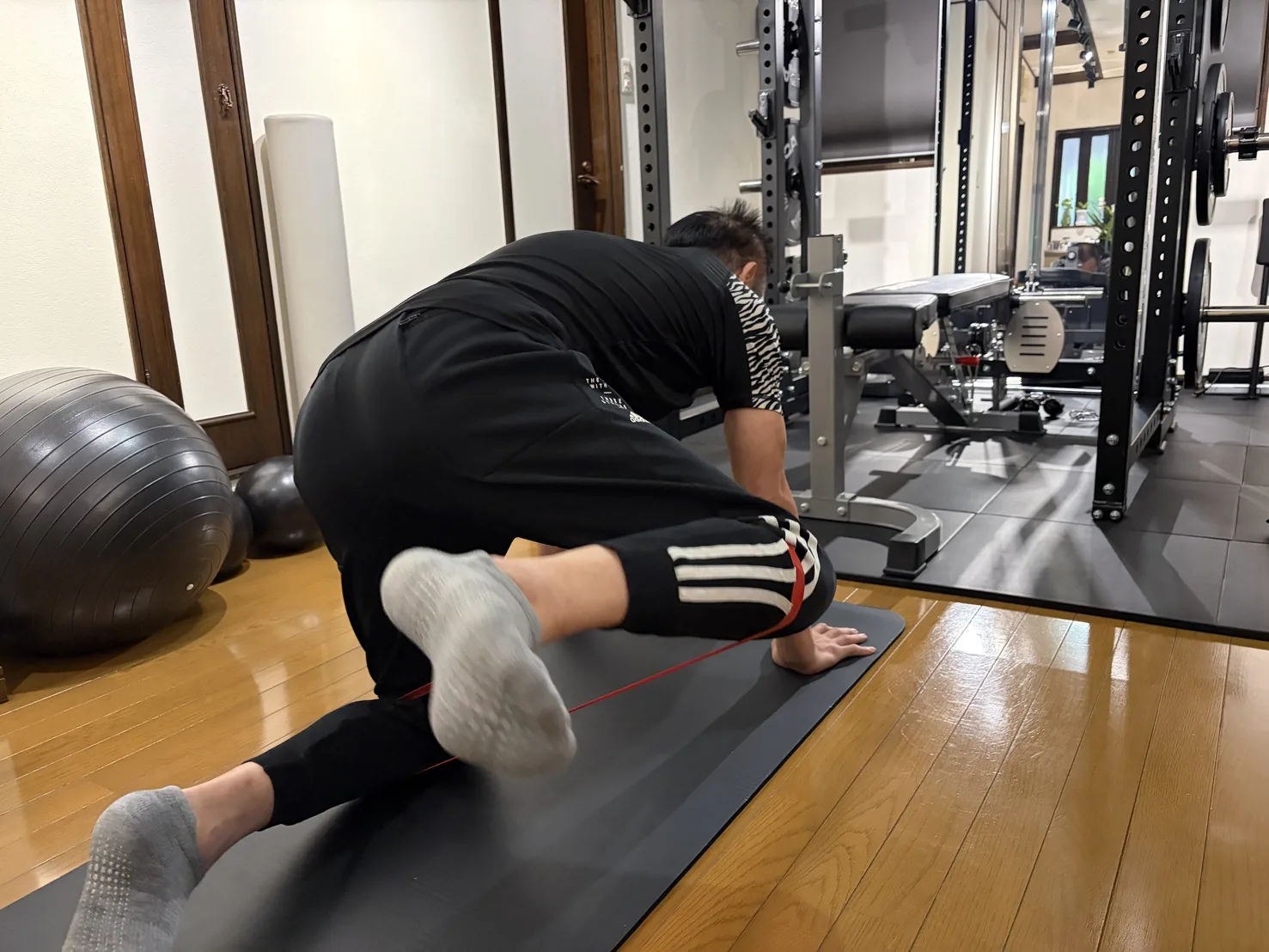 自宅のホームジムで、ゴムバンドを使ったストレッチをトレーナーが補助している様子