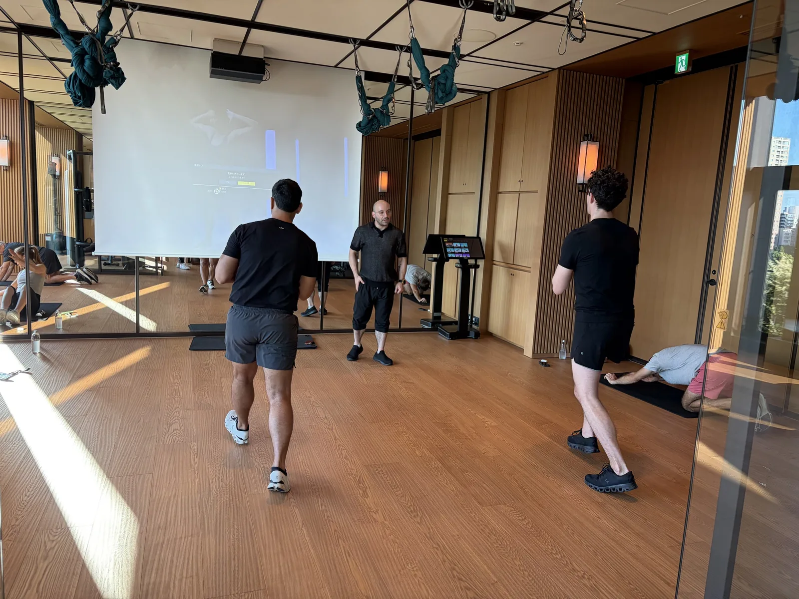 A trainer coaching two guests through a standing exercise in a hotel gym studio