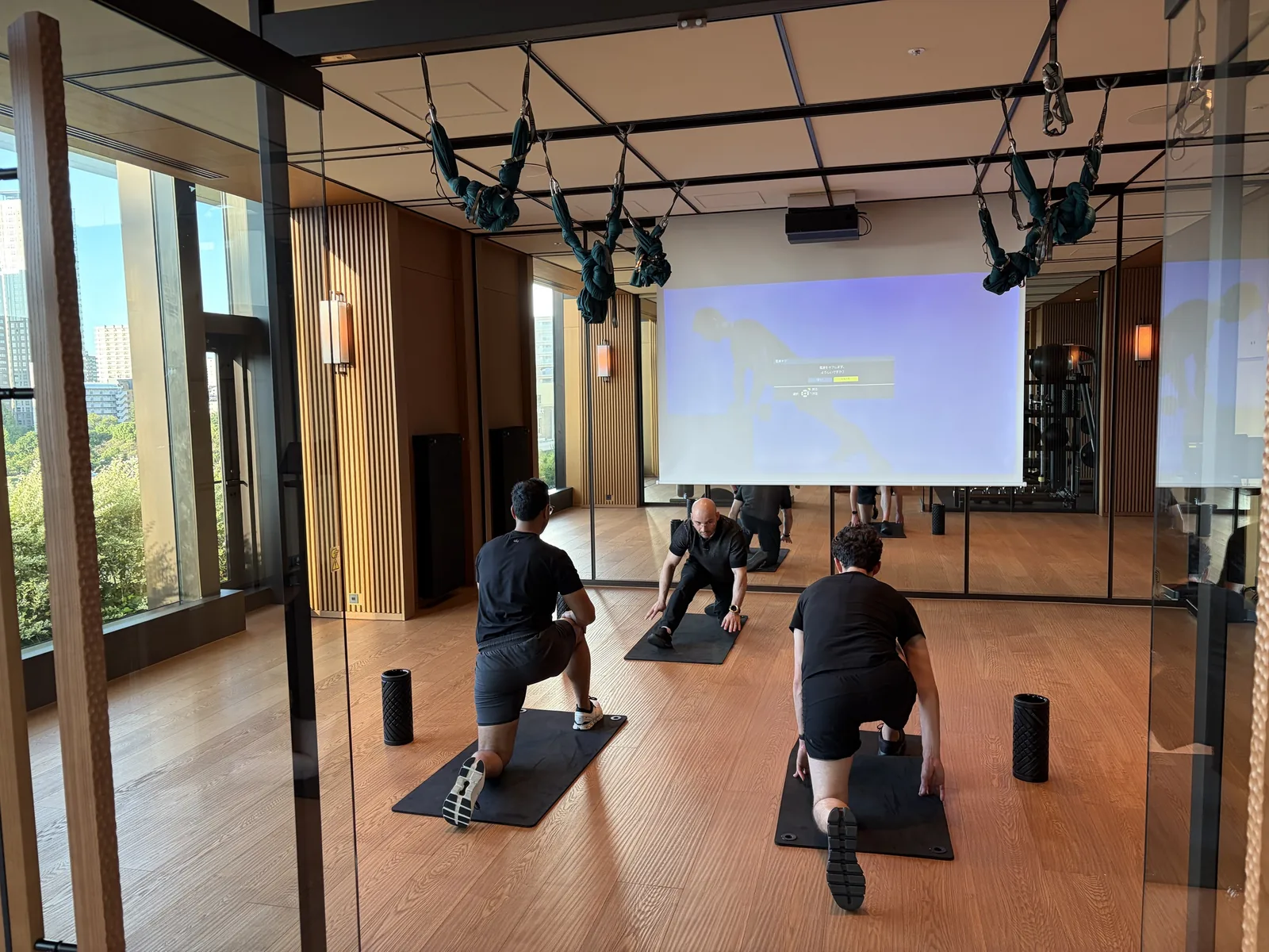 A trainer demonstrating a hip stretch on a mat while two guests follow