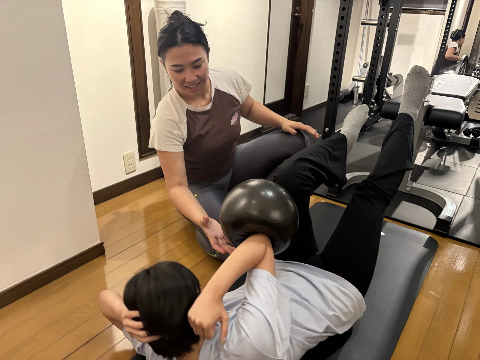 ボールを使った腹筋の種目を、女性トレーナーが手を添えて補助している様子