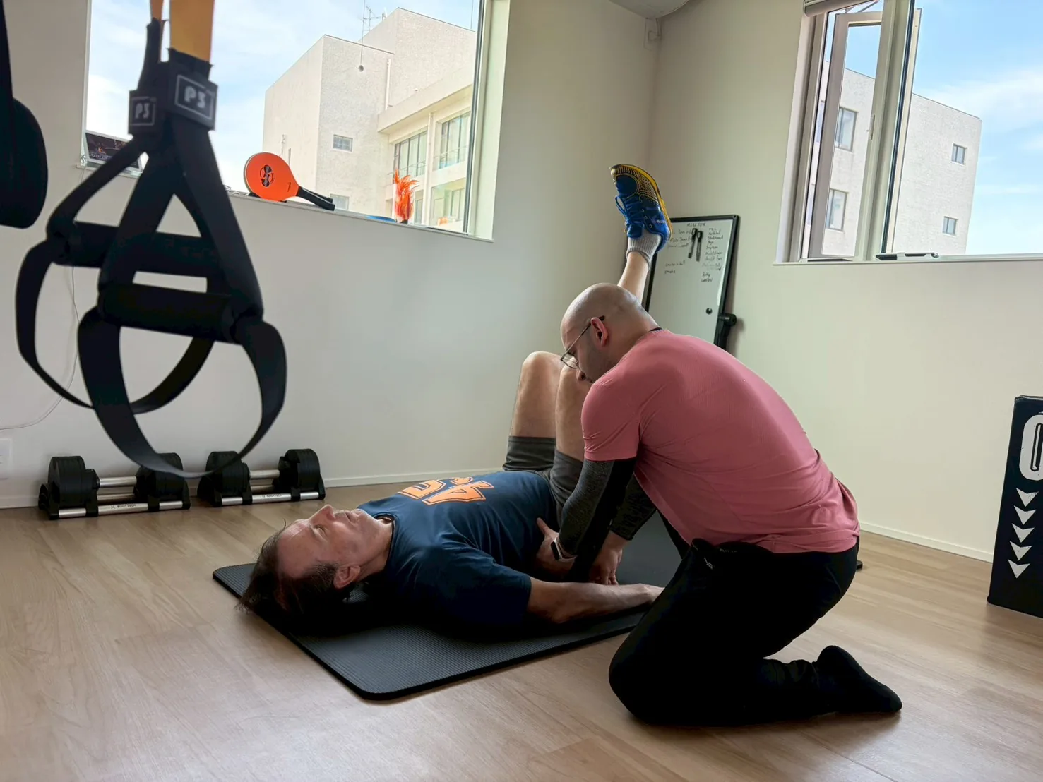 English-speaking trainer giving hands-on guidance as a client performs a guided stretch on the mat