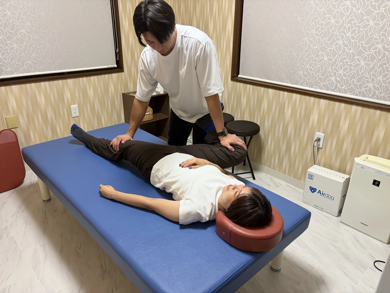 FIT STAGEのトレーナーが、仰向けの姿勢で脚のストレッチを補助する様子