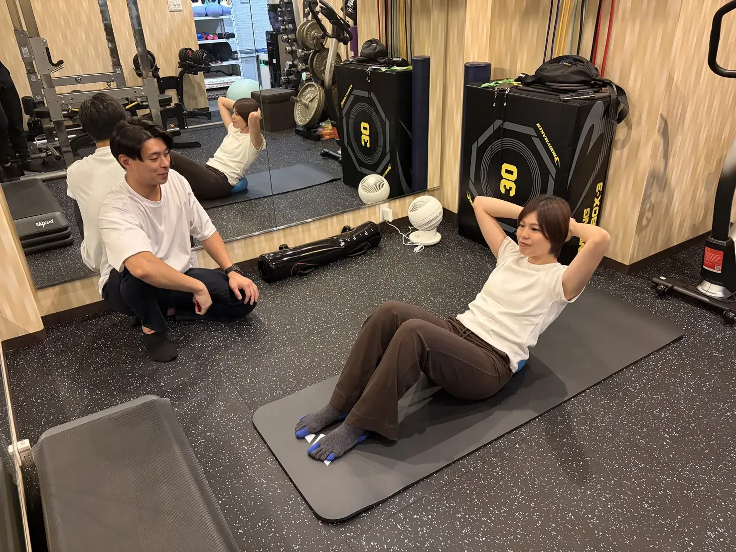 FIT STAGEのトレーナーが、マットの上での体幹種目を隣で見ながら指導する様子