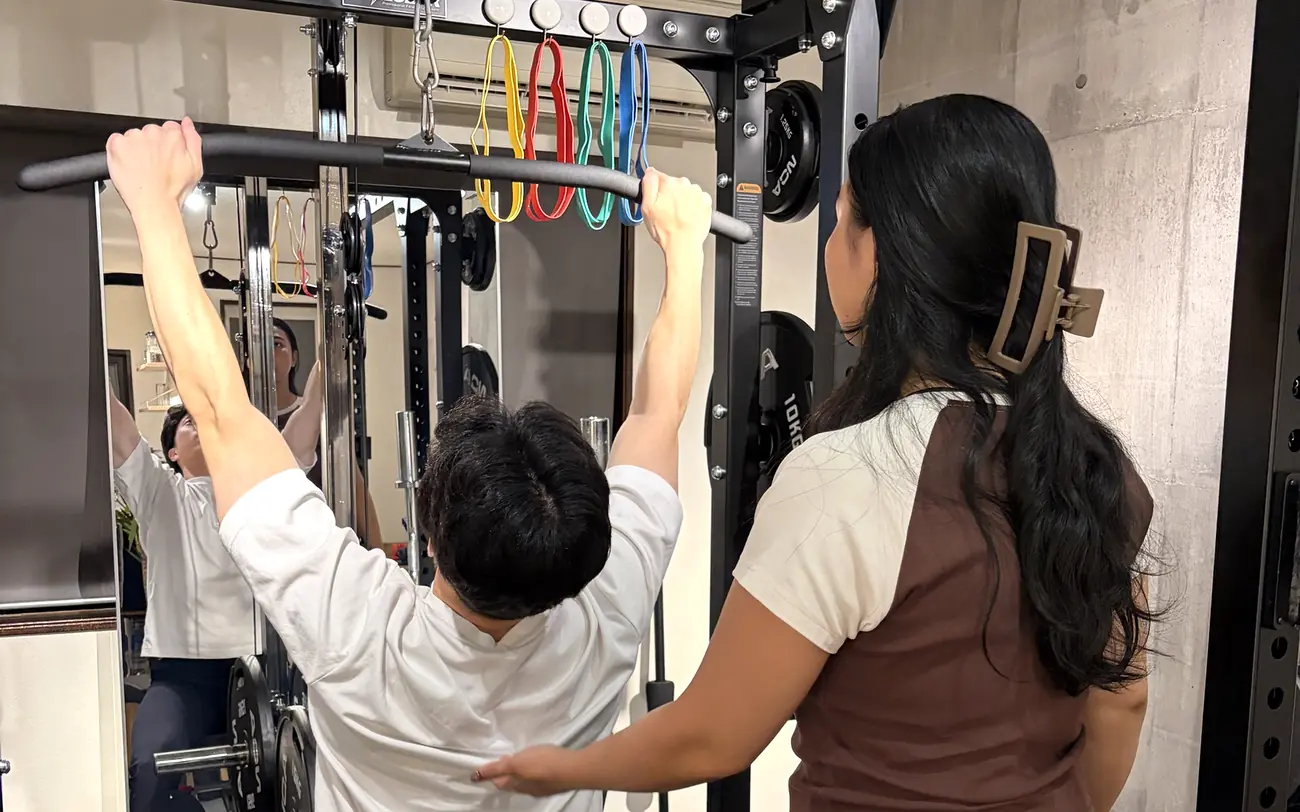 FIT STAGEのトレーナーが、ラットプルダウンのフォームを確かめながら指導する様子