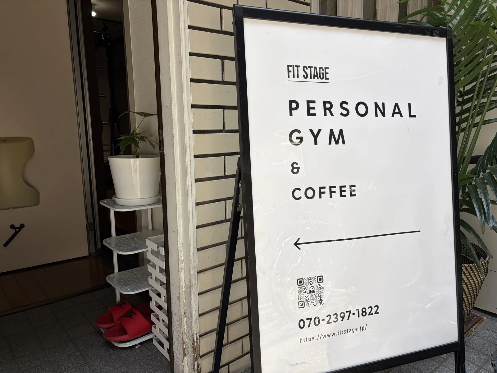 FIT STAGE 江坂店の入口に立つ「PERSONAL GYM & COFFEE」の看板。1F路面店で、段差なく建物の入口からそのまま入れる