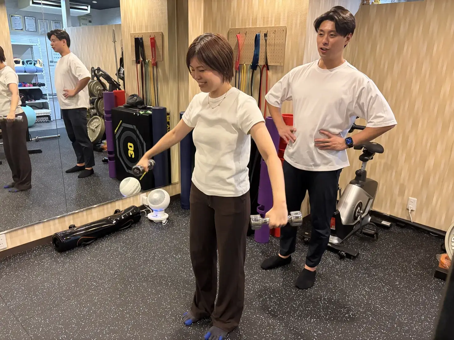 FIT STAGE 庄内店で、ダンベルを持った動作をトレーナーが隣で確認しながら指導する様子