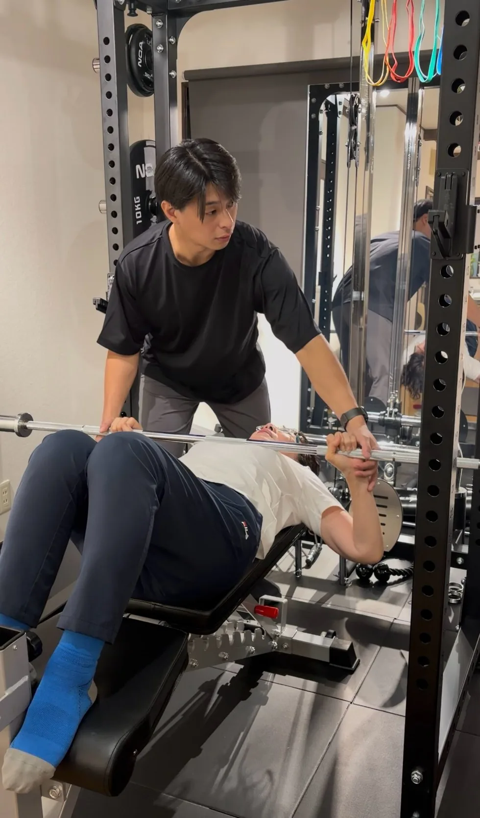 トレーナーがバーに手を添えて補助しながら行うトレーニング指導の様子