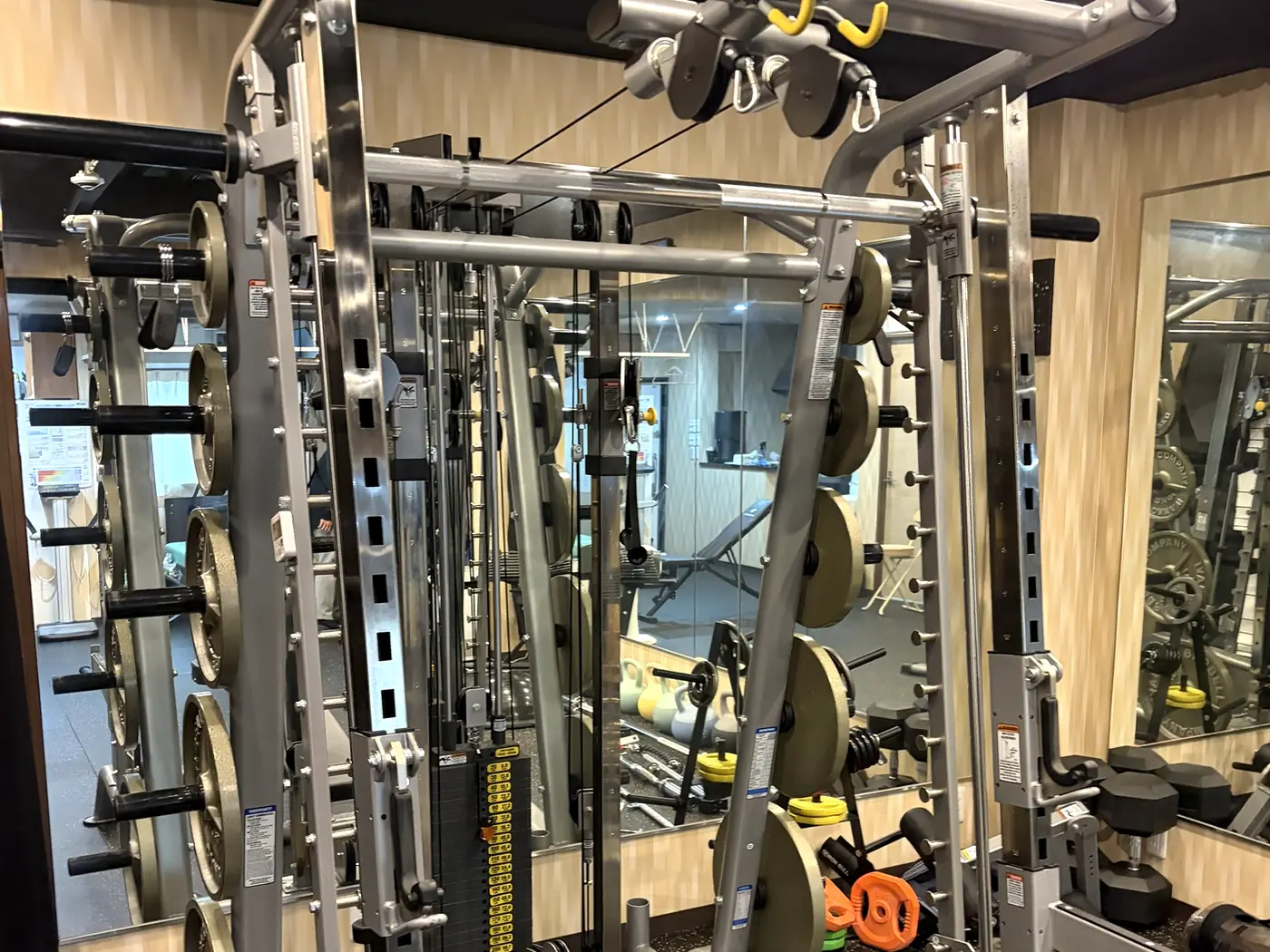 FIT STAGE 曽根城山店のスミスマシン・ケーブルマシン一体型ラック。ウエイトスタックとラットプルダウン、バーベルプレートを備える